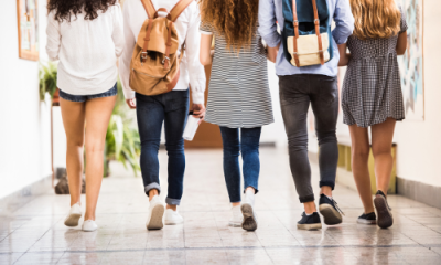 five female and male high school students walking down a hallway